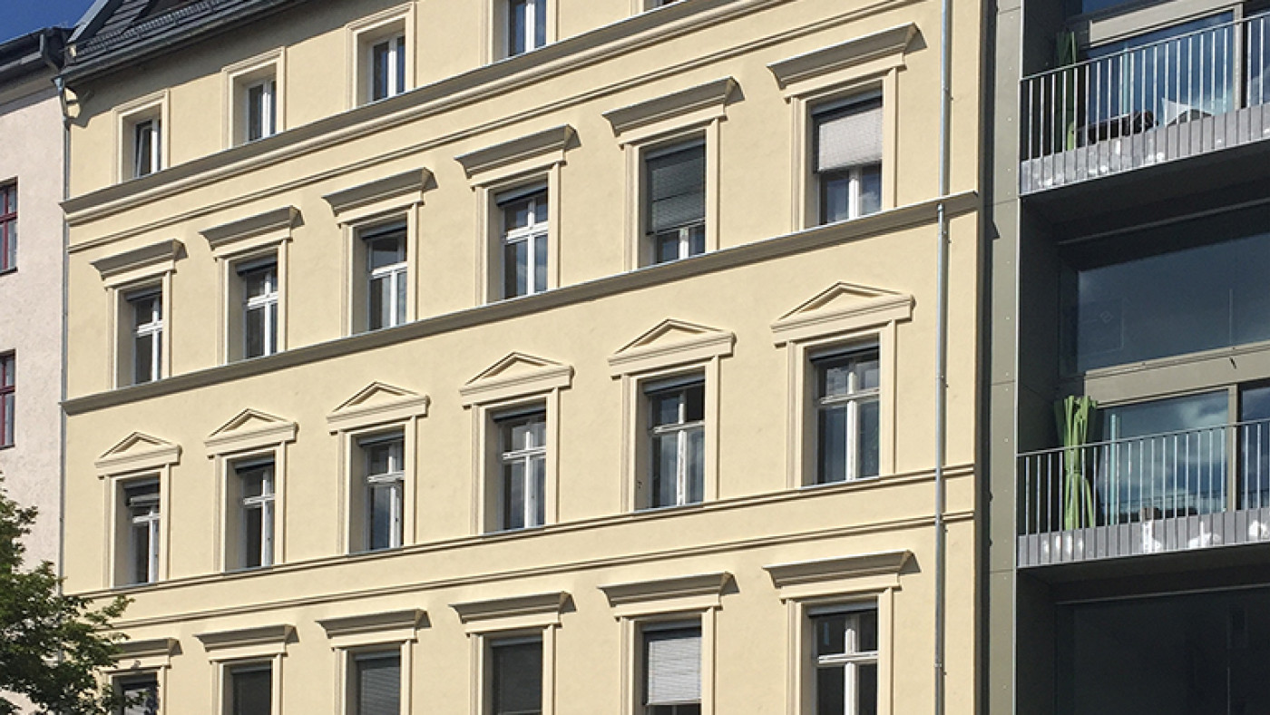 Refurbished Gr&uuml;nderzeit fa&ccedil;ade with a newly added top floor, a new building with balconies to its right.
