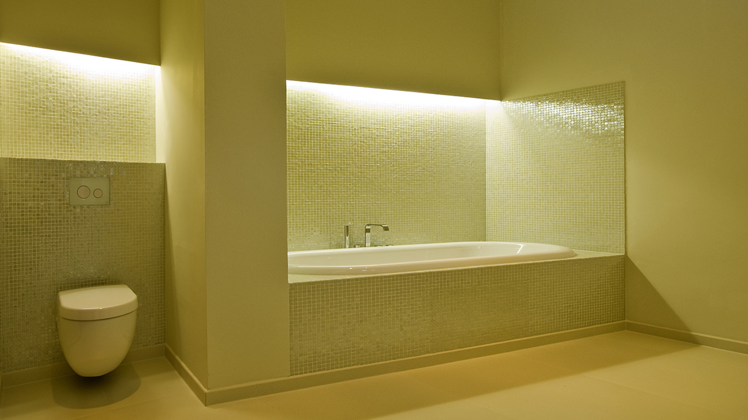Bad mit Mosaikfliesen, in eine hinterleuchtete Nische gesetzter Wanne und wandh&auml;ngendem WC.