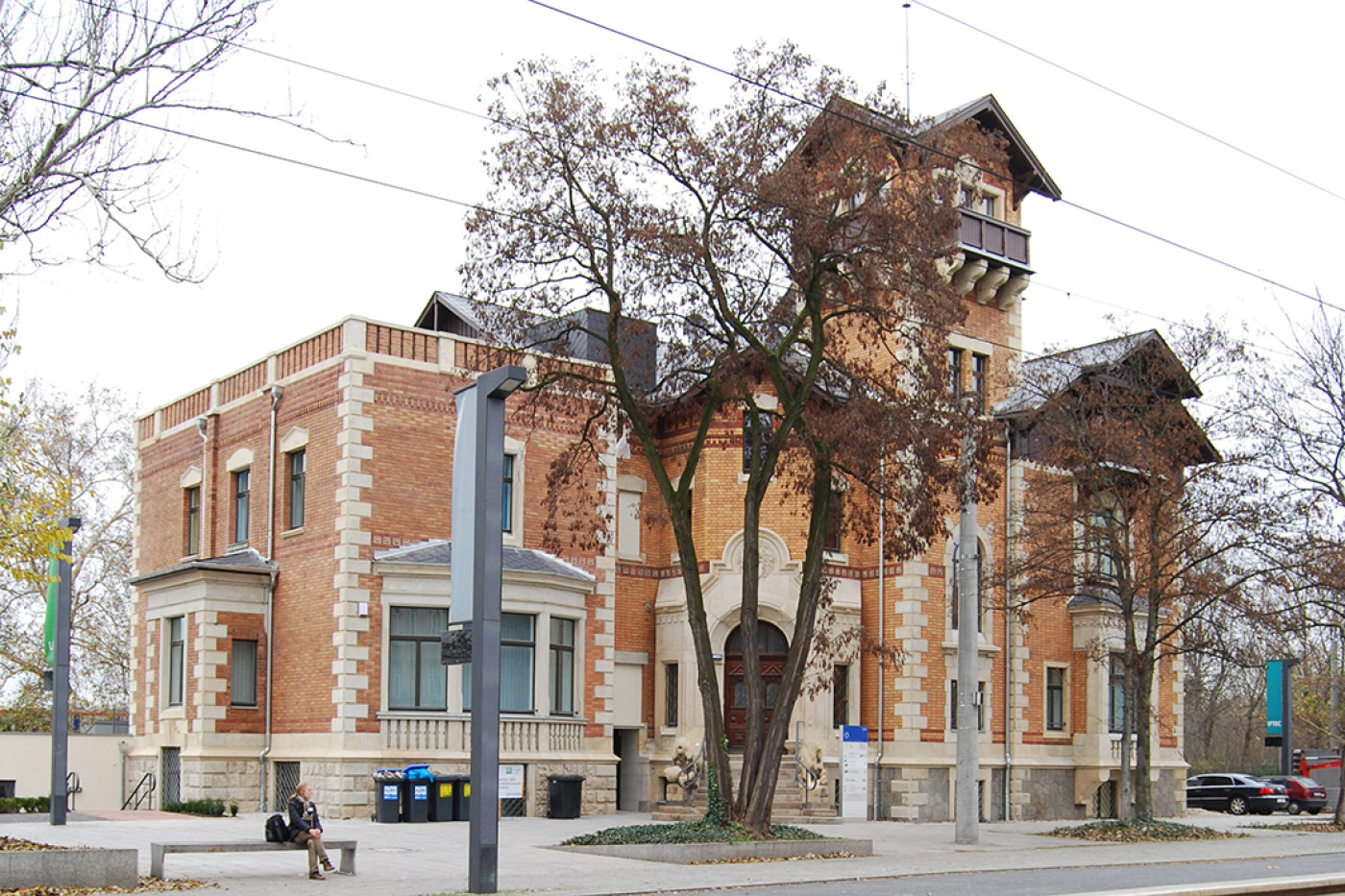 Die Villa an der Stra&szlig;enecke mit Klinkerfassade, hellen Sandsteinkanten und Eckturm, davor kahle B&auml;ume.