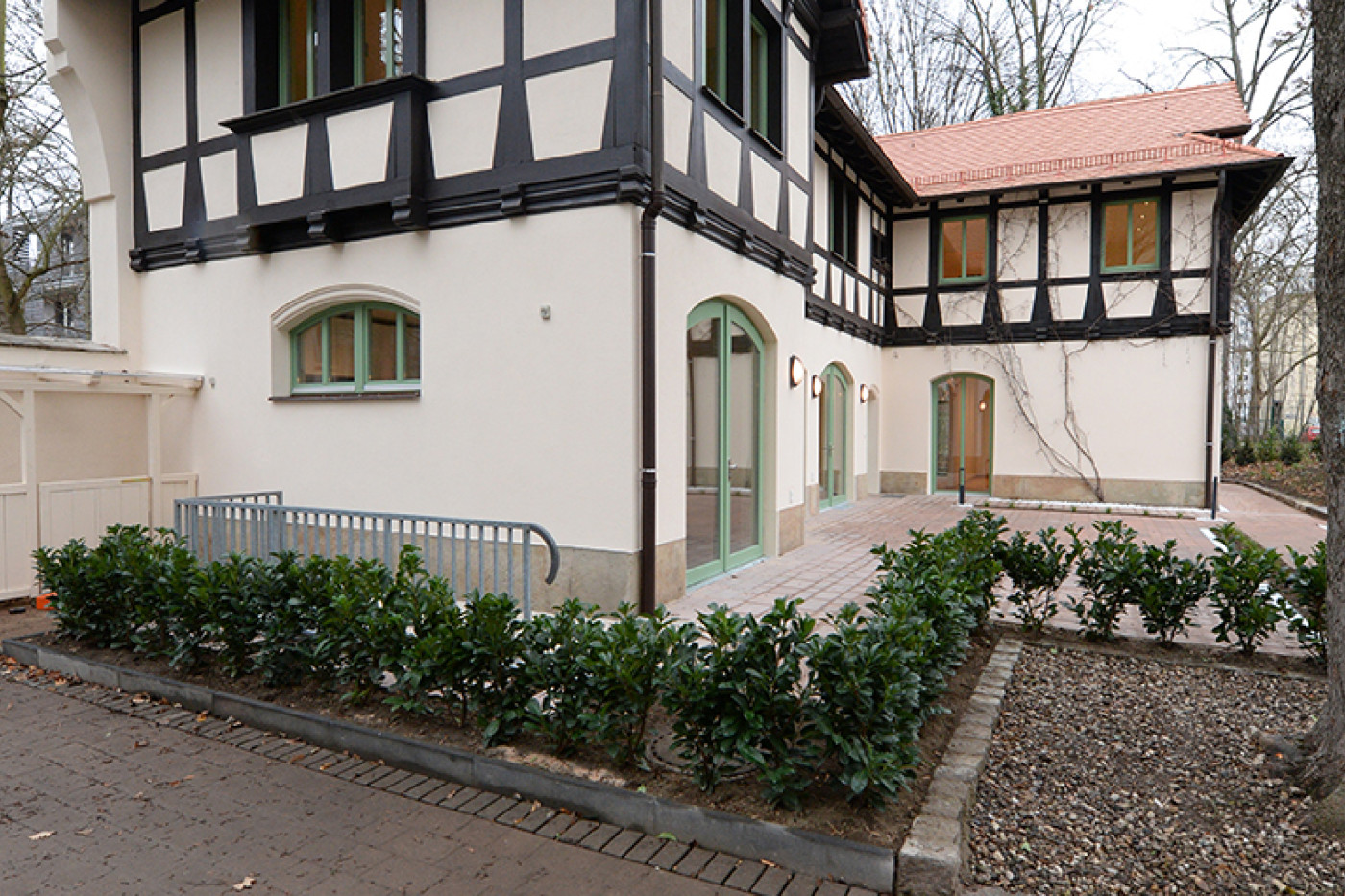 Gable end of the villa with a projecting half-timbered upper floor, a hedge and gravel bed in front.