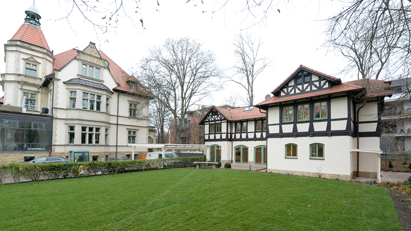 Listed villa with a tower, the coachman's house with a half-timbered gable to its right, a lawn in front.