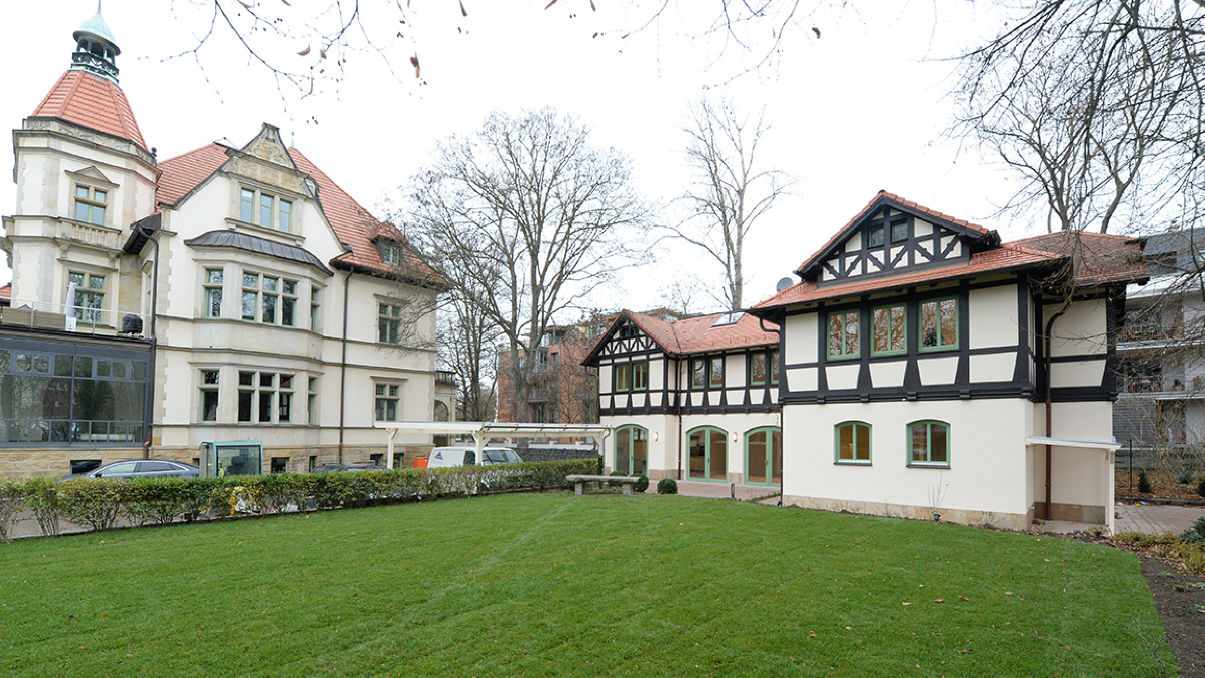 Listed villa with a tower, the coachman's house with a half-timbered gable to its right, a lawn in front.