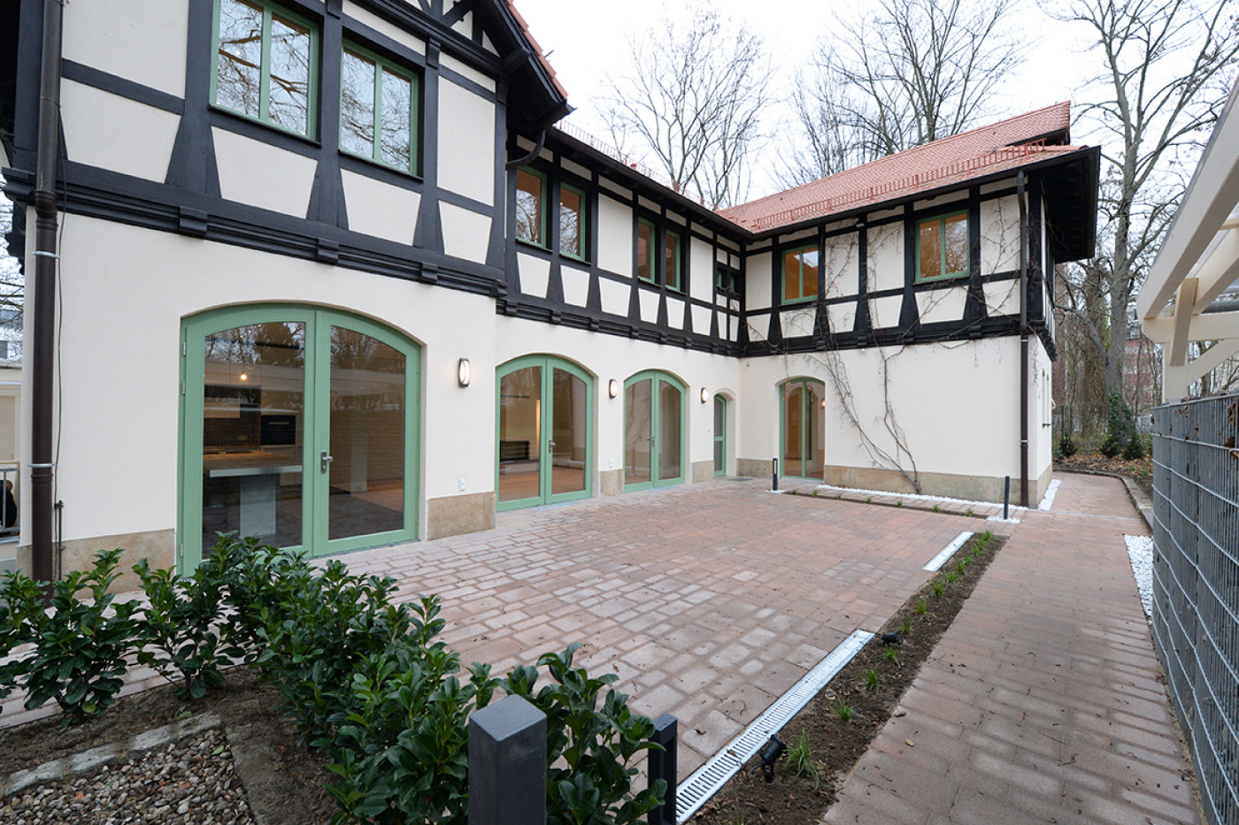 The paved courtyard along the half-timbered fa&ccedil;ade with green-painted arched doors and newly planted hedges.