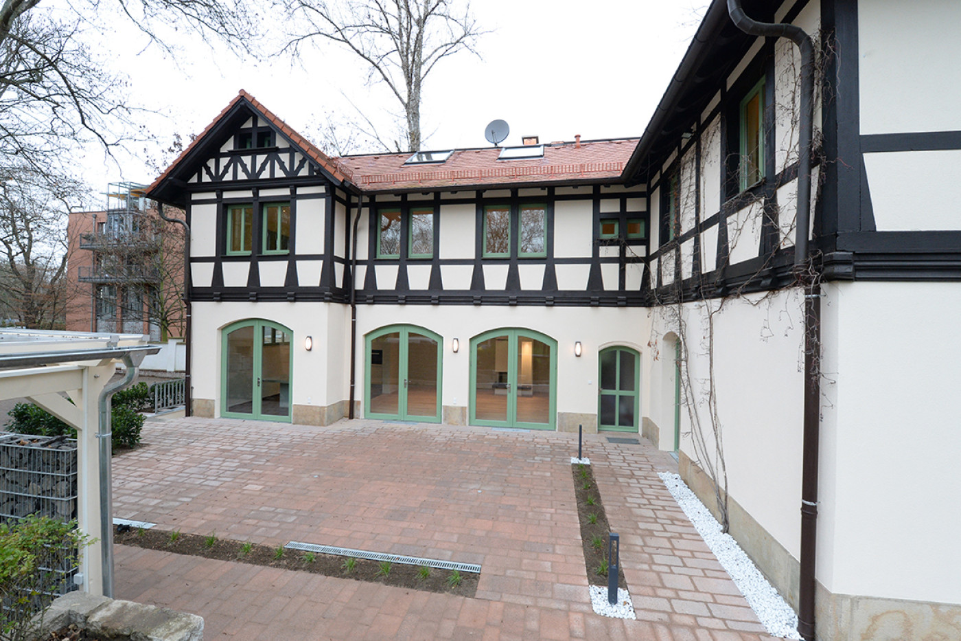 Courtyard between the villa and the coachman's house with a paved surface and green-painted round-arched doors.