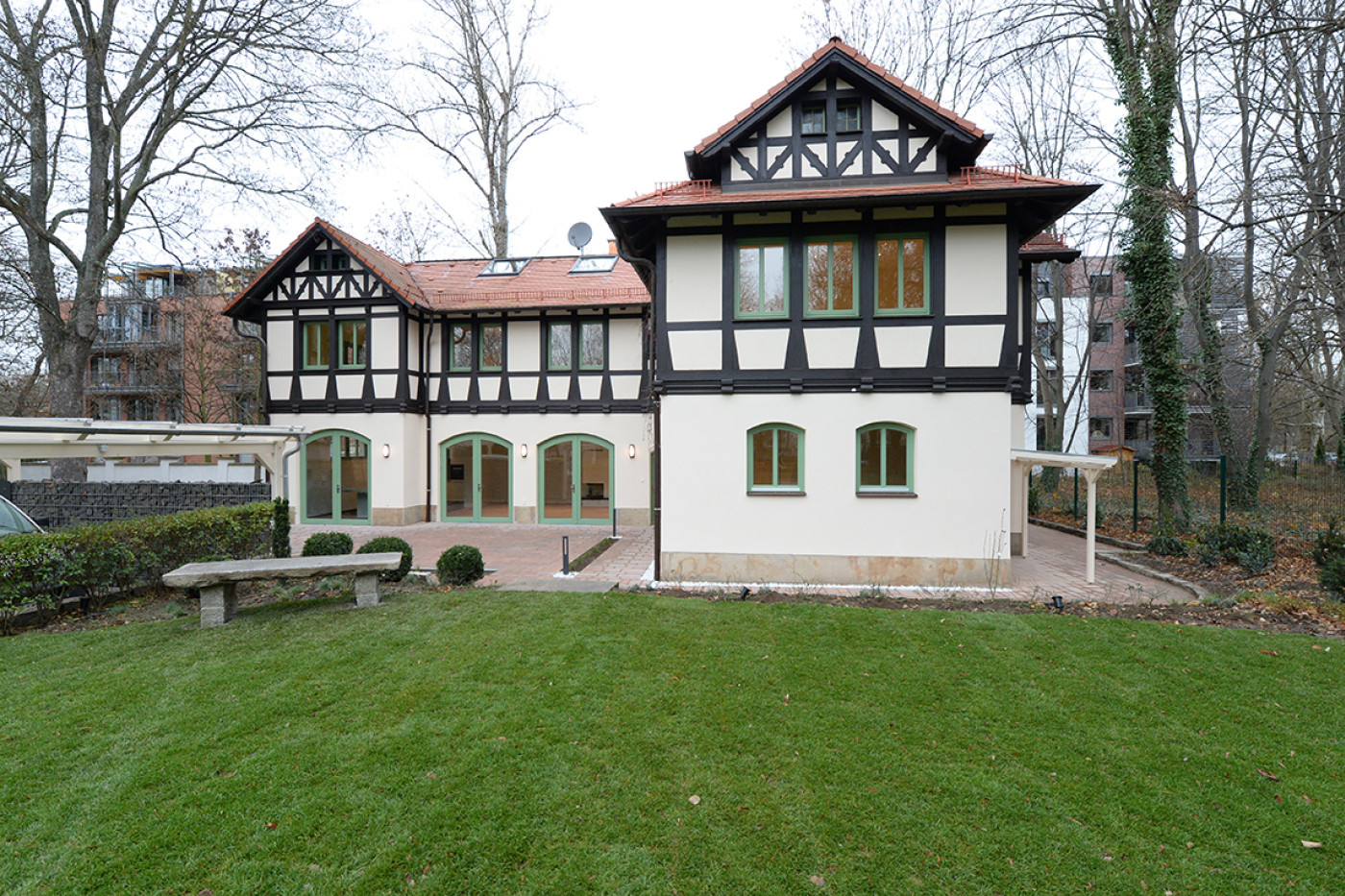 The refurbished villa with half-timbered gables and a red tiled roof from the garden side, a large lawn in front.