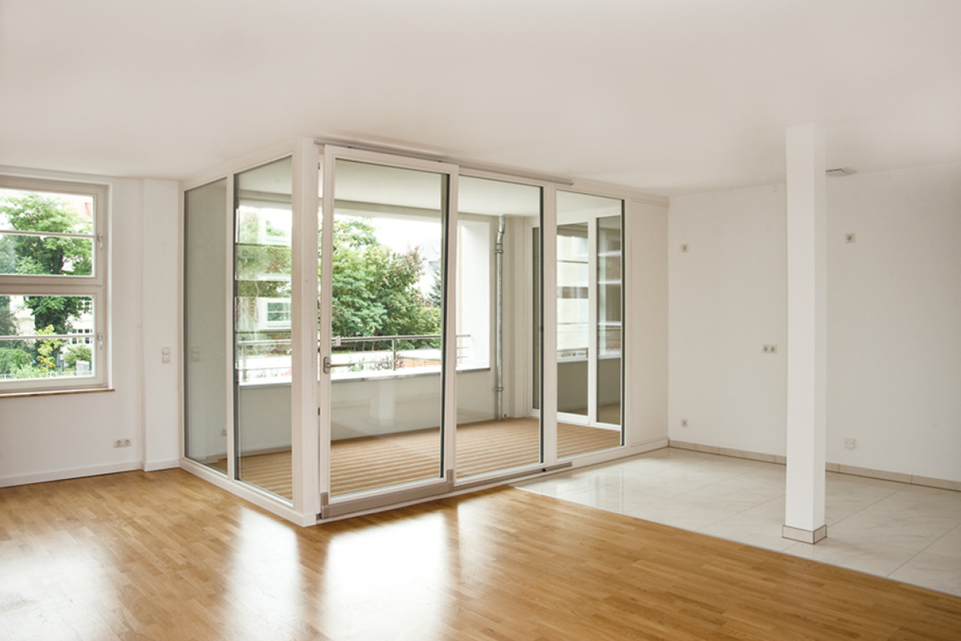 Empty bright living room with a parquet floor, a glazed corner loggia and a free-standing column.