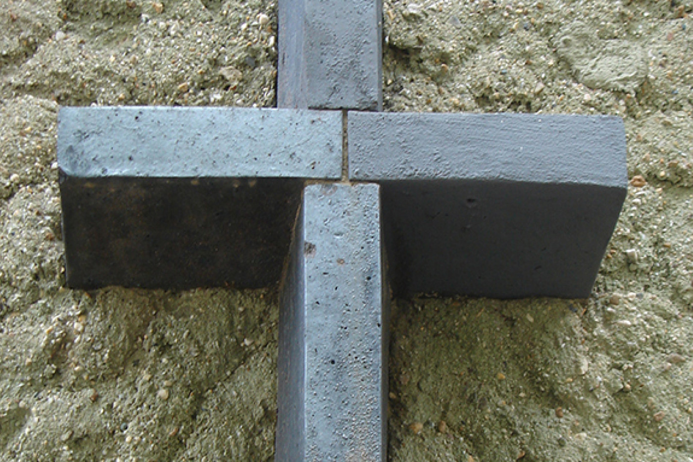 Close-up of a cross-shaped metal anchor on rough greenish render.