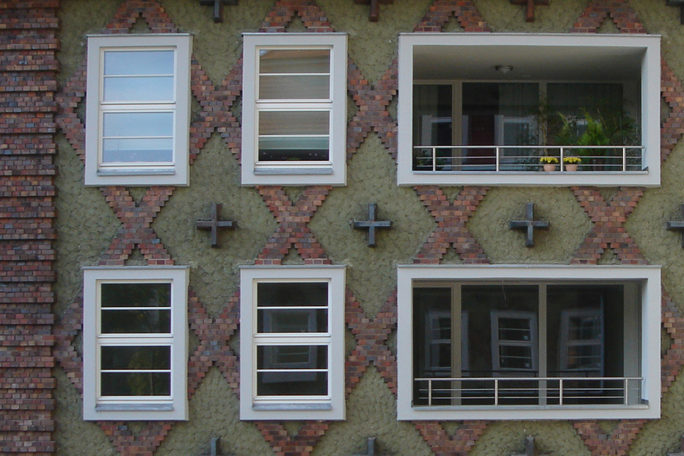 Section of fa&ccedil;ade with white windows and a recessed loggia, cross-shaped anchors set into the diamond pattern between them.