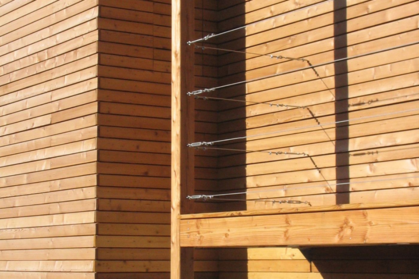 Detail of the timber fa&ccedil;ade with a vertical post and tensioned wires as a climbing frame, the concrete plinth below.