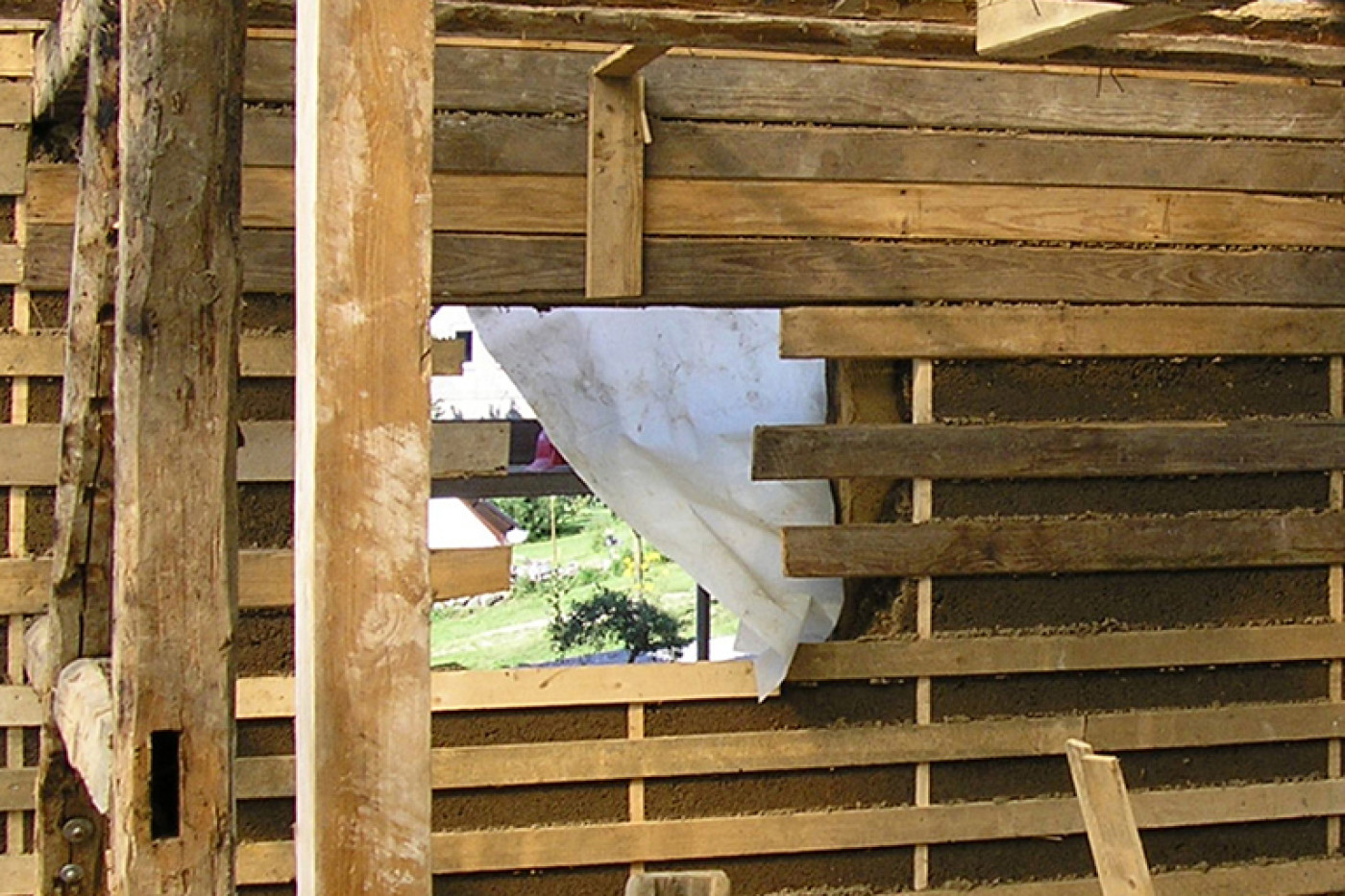 Exposed timber framing during the works with old beams, new battening and a view outside.