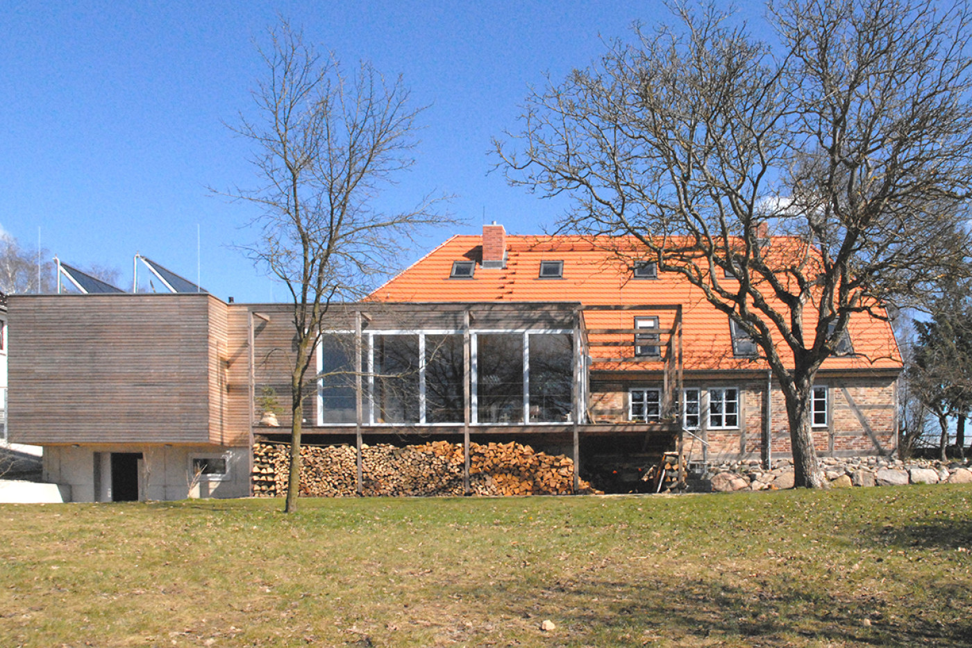 The converted inn seen from the meadow: red tiled roof, a glazed extension and the timber-clad new section on the left.