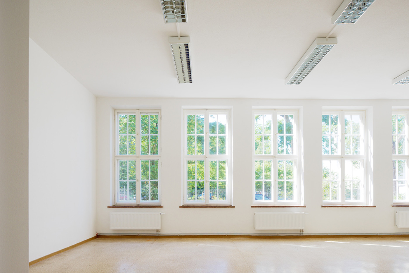Empty bright room with four tall glazing-bar windows and fluorescent fittings on the ceiling.