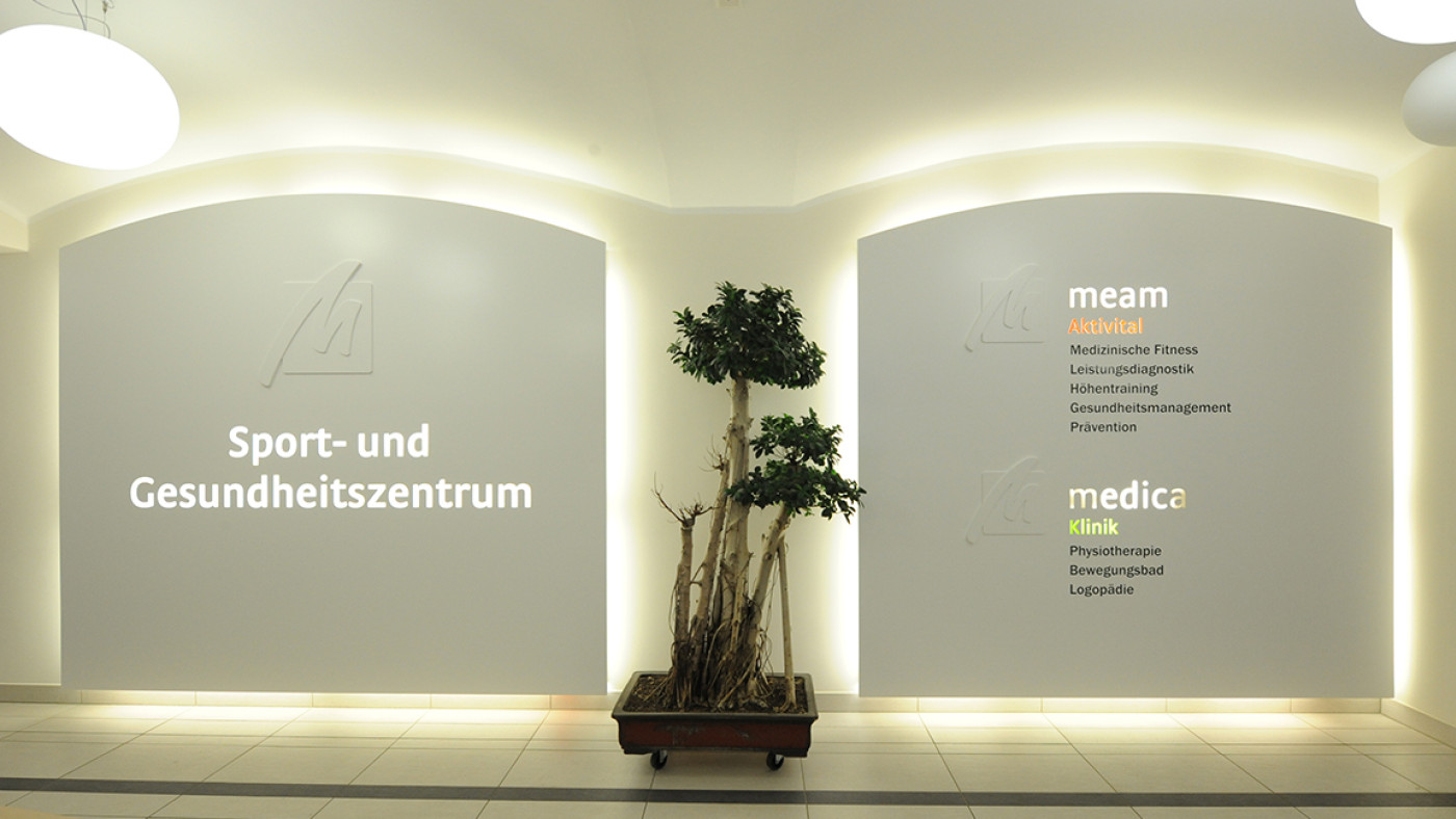 Foyer with backlit signage panels set into the wall niches and a topiary shrub in front.