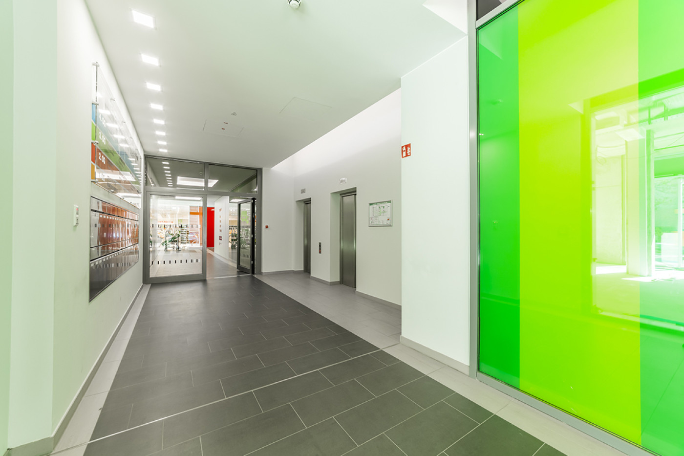 Corridor with a bright green glass wall on the right and framed pictures on the left-hand wall.