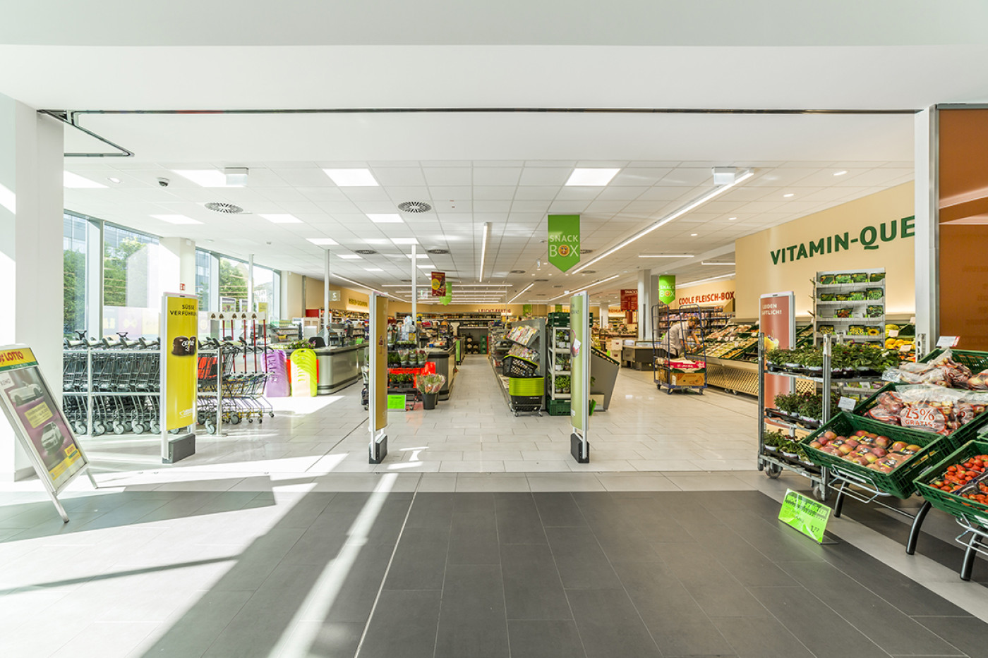 Sales floor with fruit and vegetable displays, the checkout area and signage hanging from the ceiling.