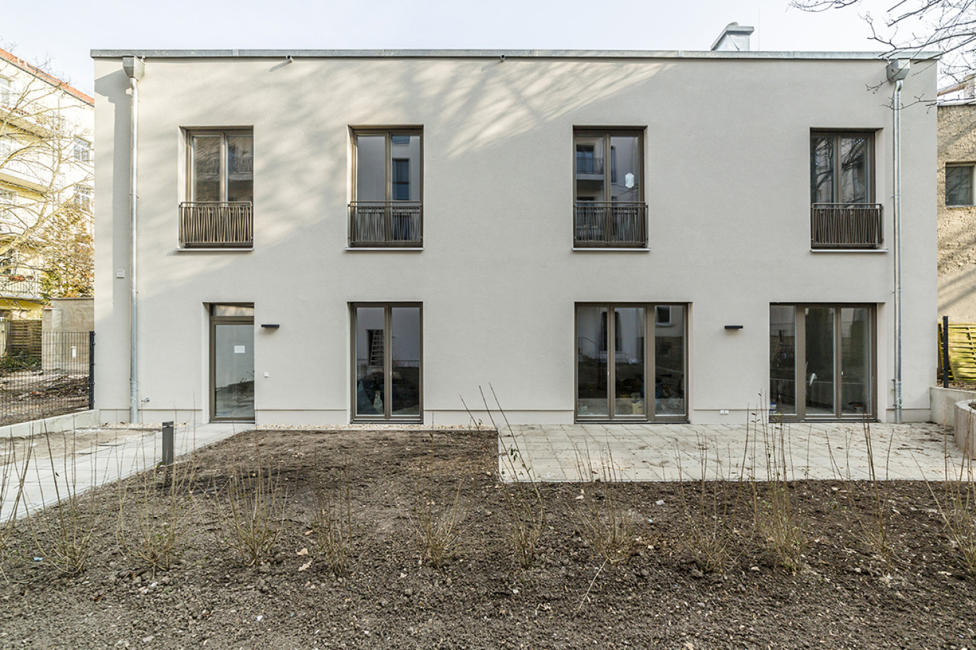 Rear of the new building in pale render with balconies and floor-to-ceiling windows, the garden still unplanted.