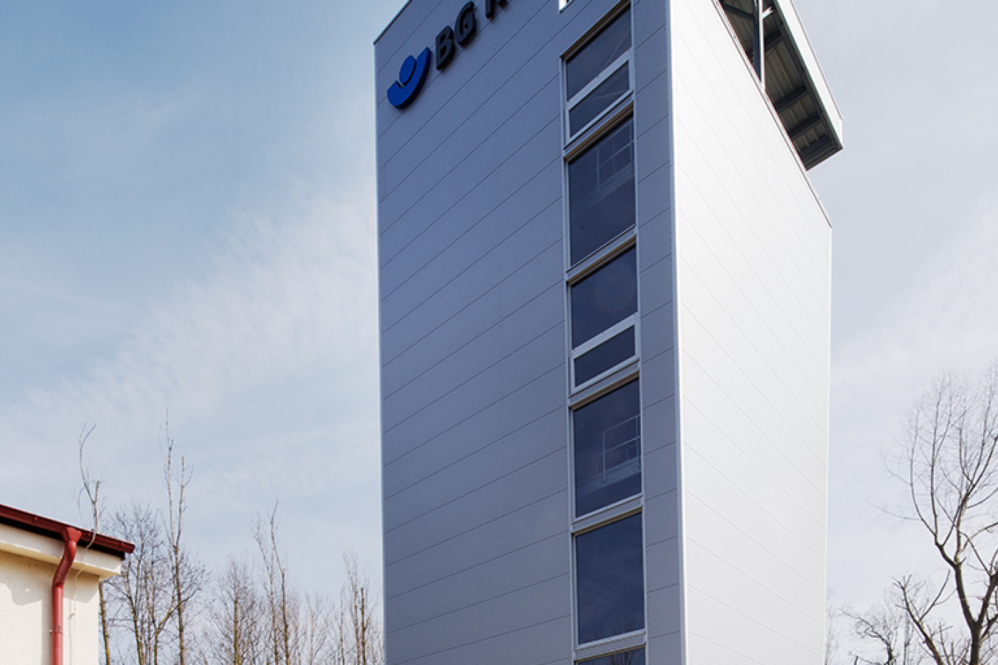 Training tower with BG RCI lettering and an open practice platform, trainees in orange protective clothing in front.